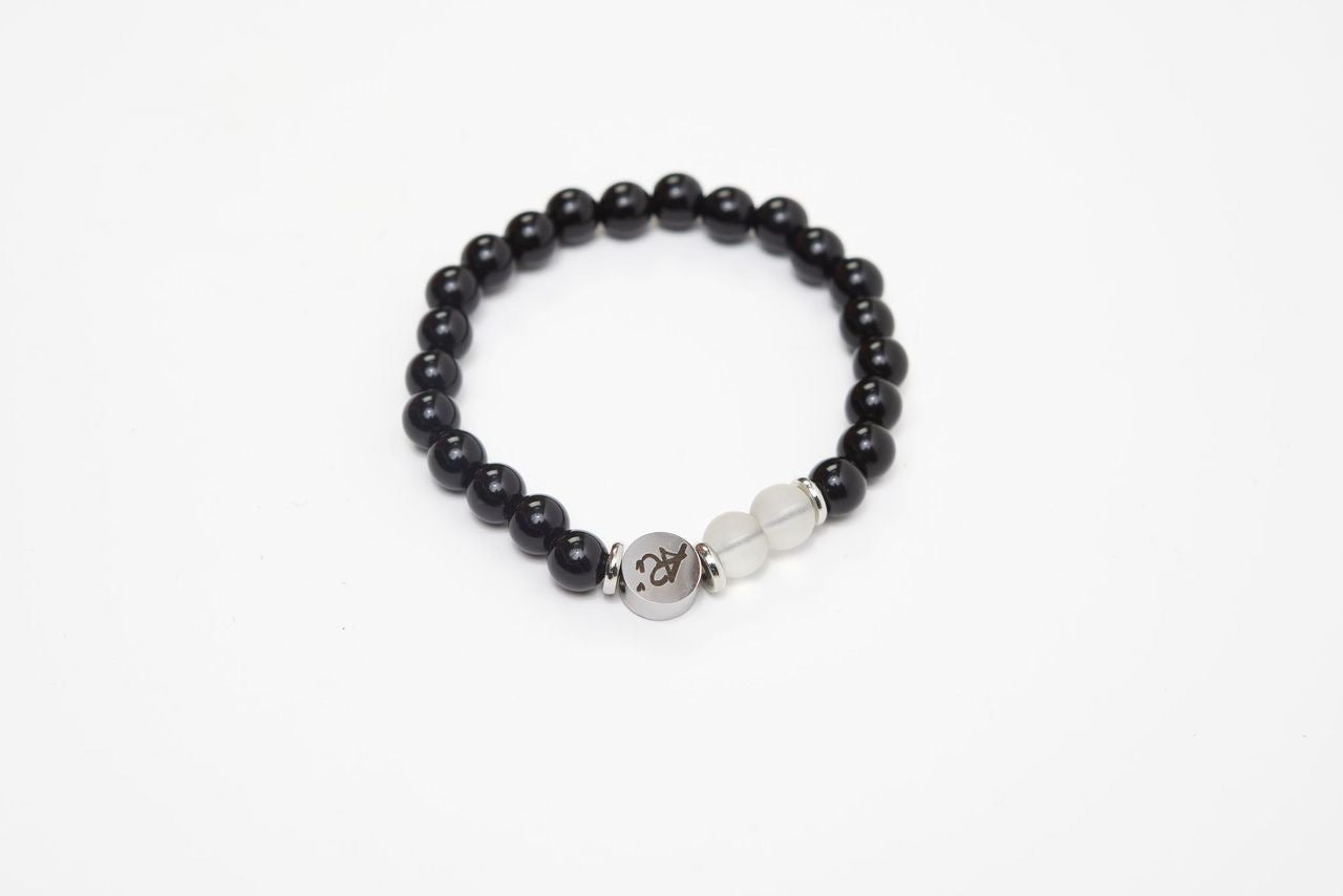 Black beaded bracelet with a silver charm and two white beads on a white background.