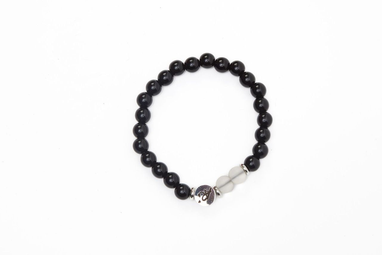 Black beaded bracelet with a silver charm and two white beads on a white background.