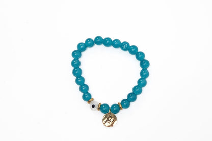 Teal beaded bracelet with a gold charm, gold accents, and a single white bead with a black dot on a white background.