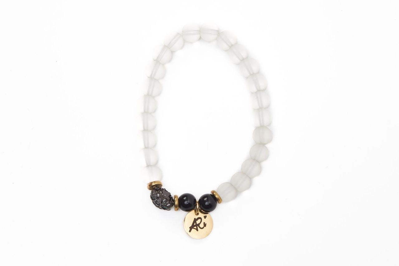 White beaded bracelet with gold accents, black beads, and a gold charm on a white background.